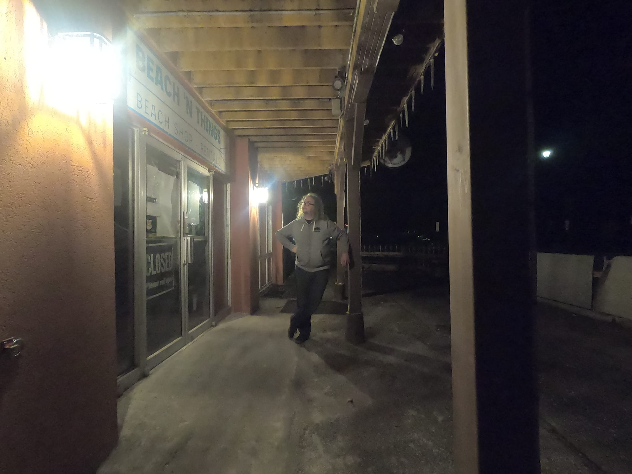 A man with green hair leans against a support post at night